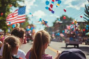 Patriotic parade with US flag and float in distance.